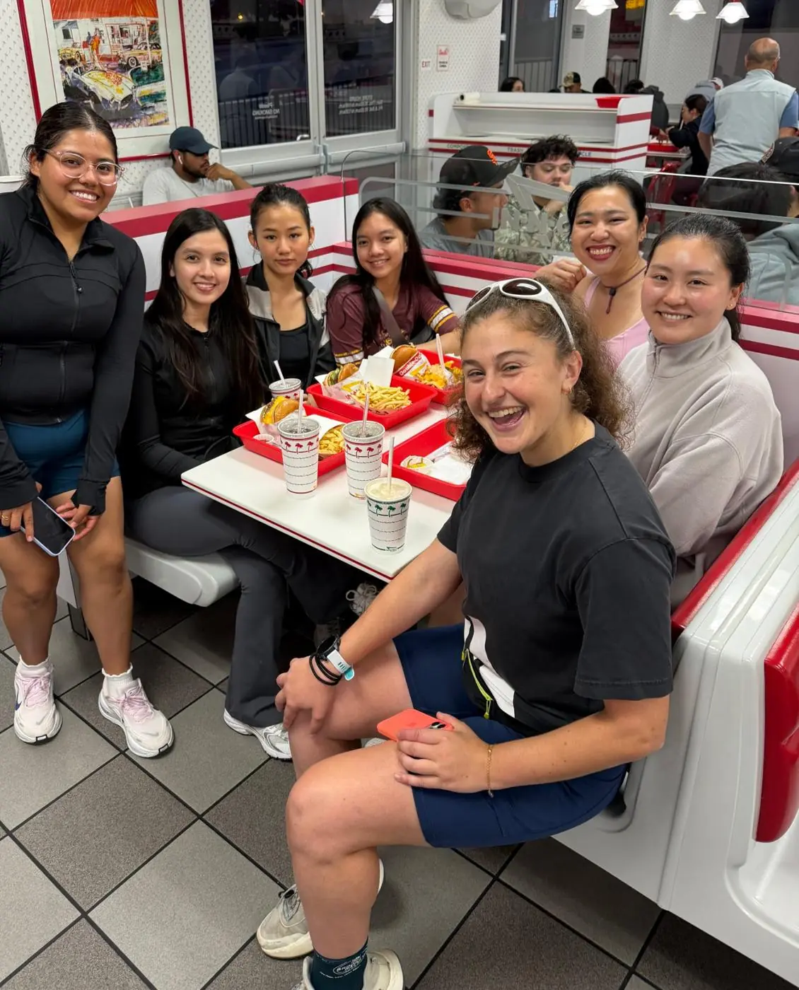 Run club friends laughing together around a booth, sharing food after a run