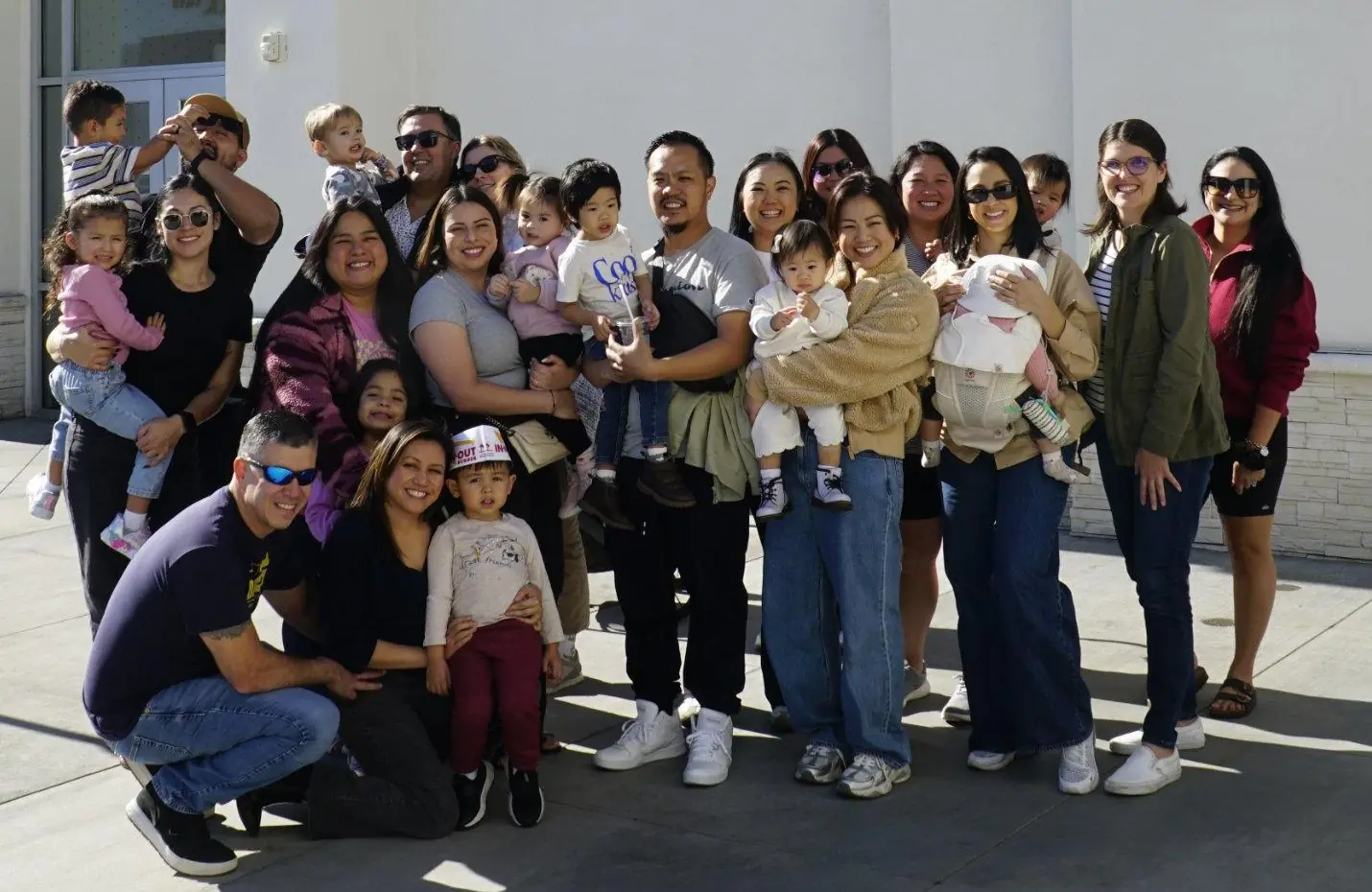 Parents and their little ones gathered together in the sunshine, toddlers held up high